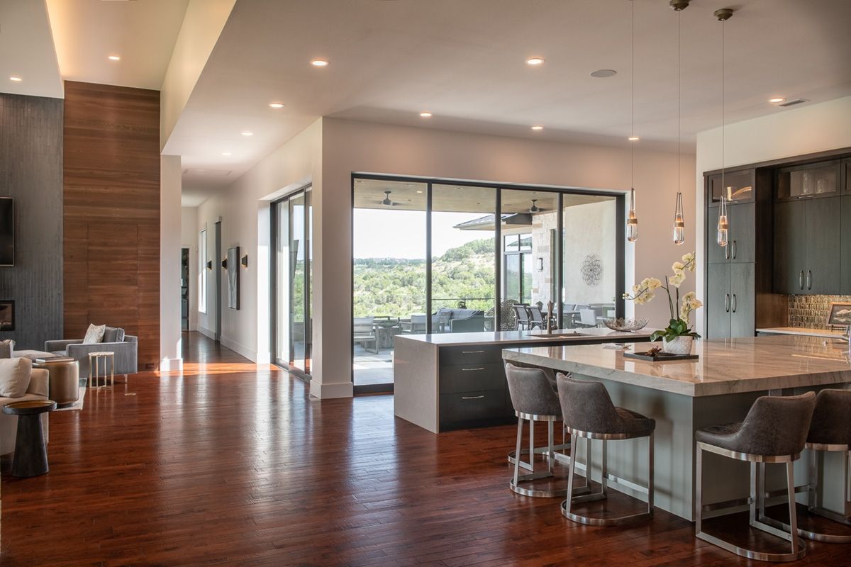 Open-concept kitchen and living area with wooden floors, large windows, and a kitchen island with bar stools.