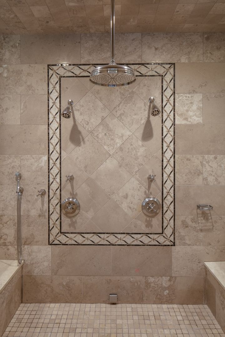 Luxurious beige tiled shower with a mosaic tile frame and multiple showerheads.