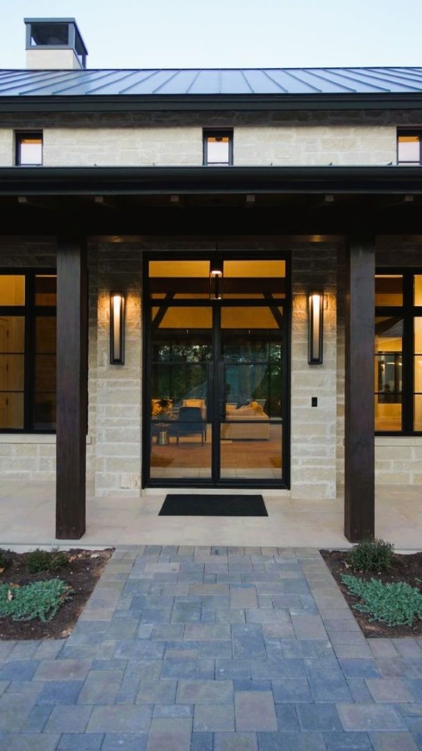 A modern house entrance with stone facade, dark wood accents, glass doors, and brick pathway.