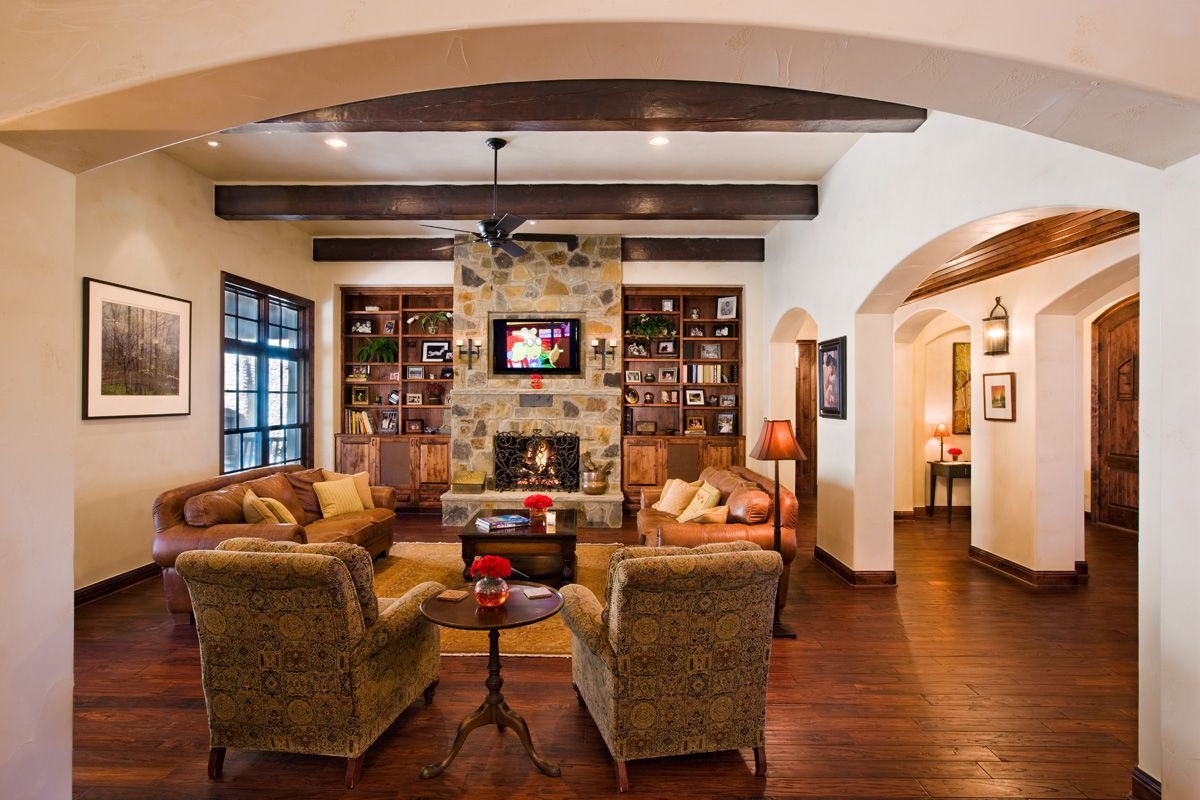 Living room with stone fireplace, built-in shelves, arched doorways, and hardwood floors.