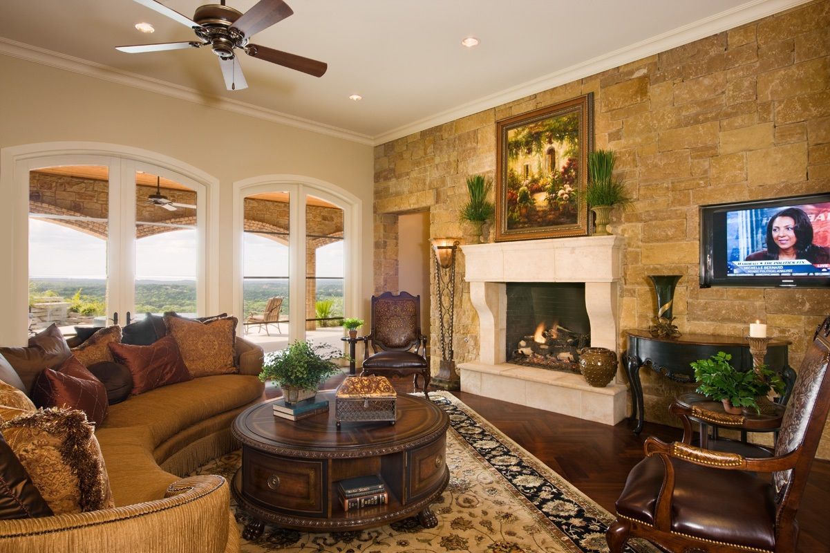 Living room with stone wall, fireplace, large windows, and brown leather furniture.