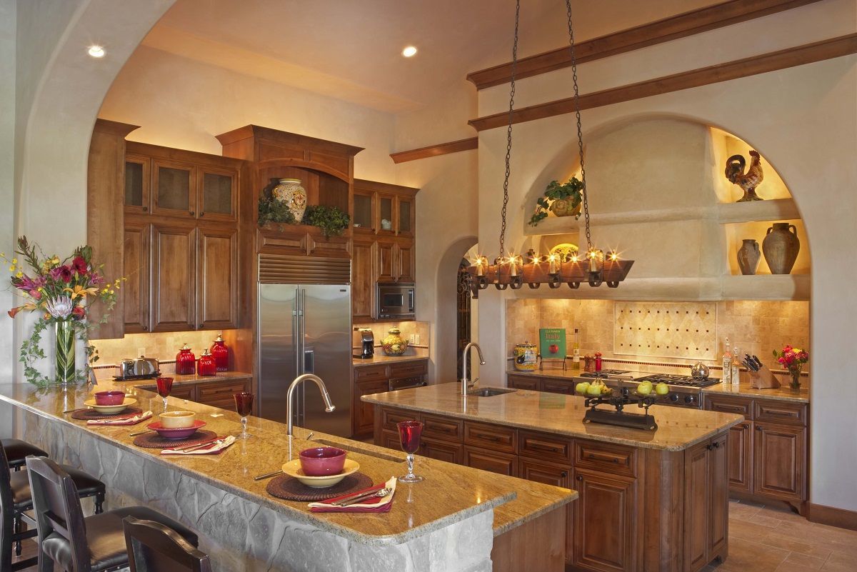Spacious kitchen with granite countertops, wooden cabinets, two islands, and an arched alcove.