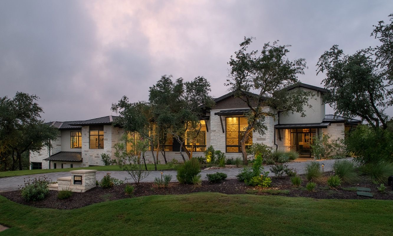 A two-story house with a stone exterior and warm interior lights at dusk.