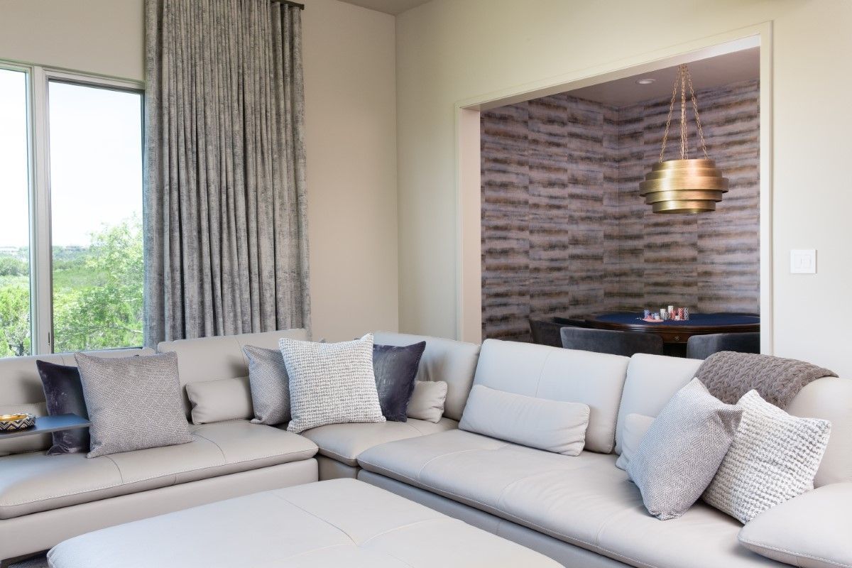 Living room with a large sectional sofa, window, and an opening to a dining area with a gold pendant light.