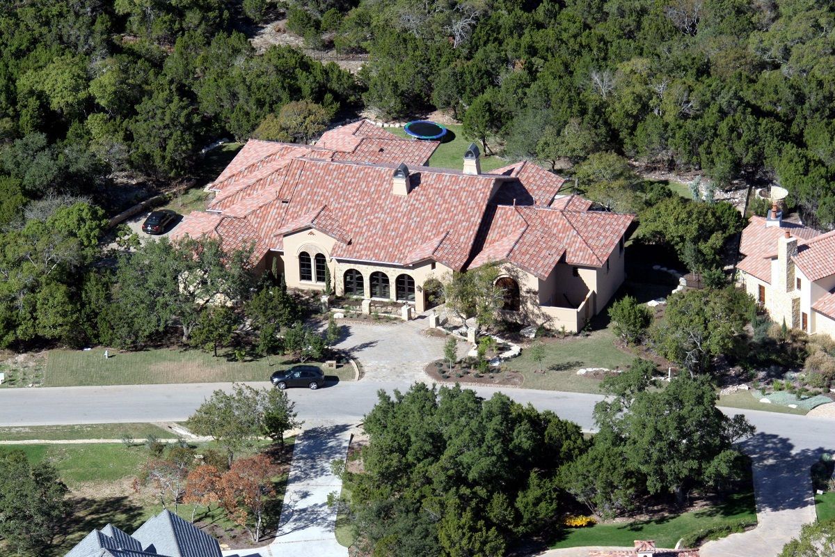 Large house with red tile roof, surrounded by trees. A car is in the driveway.