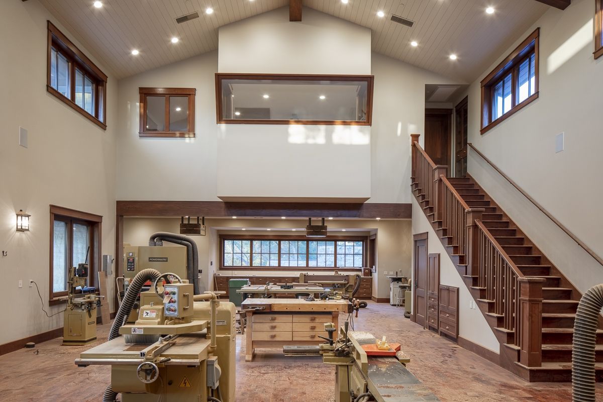 A large woodworking shop with various machines, windows, and a staircase.