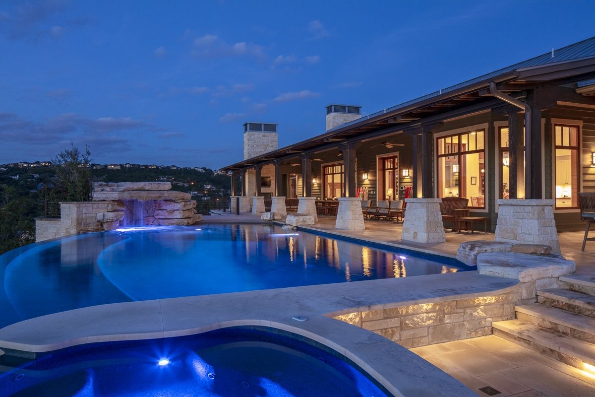 Luxury home with an infinity pool overlooking a scenic view at dusk; pool is lit with blue lights.