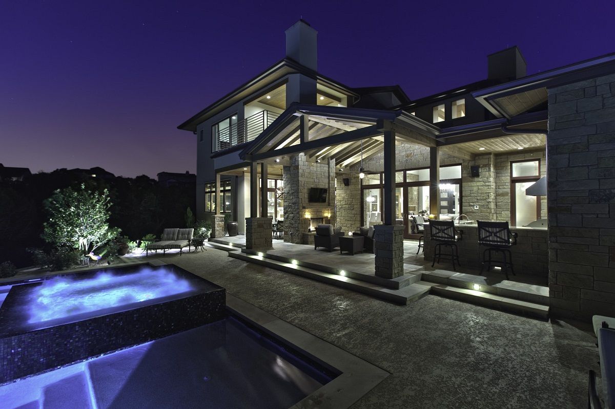 Luxury home exterior at dusk with lit pool, patio, and stone facade.