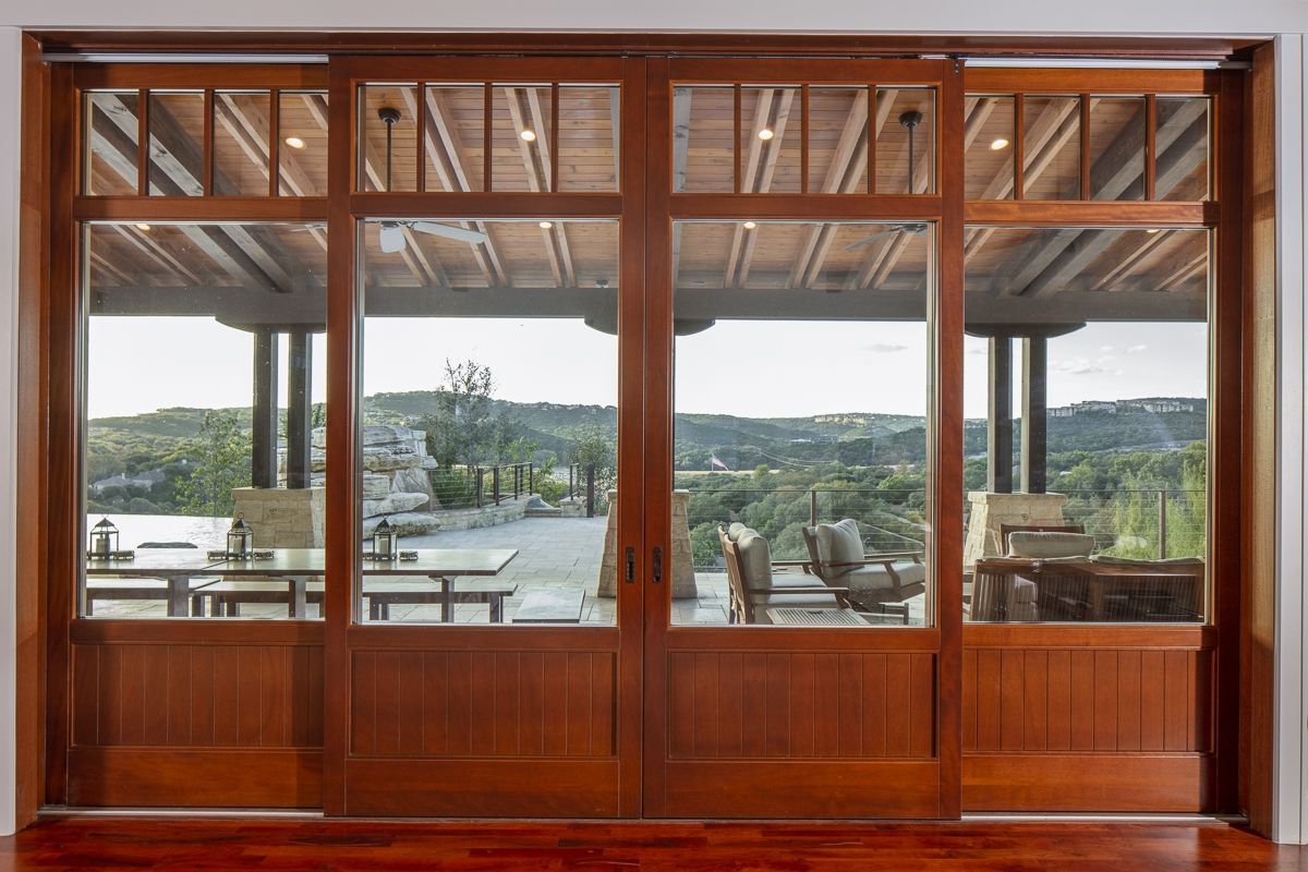 Wooden sliding doors open to a patio with scenic views of tables, chairs, and the landscape.