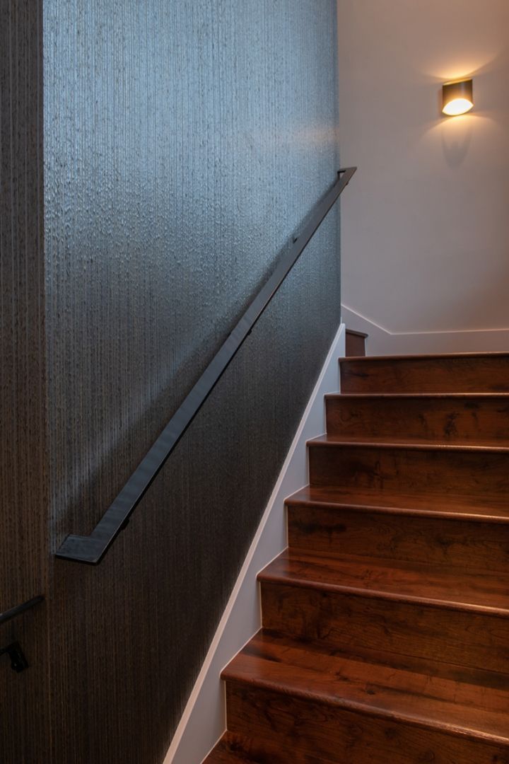 Staircase with dark wood steps, white trim, and a dark metal handrail against a textured gray wall.
