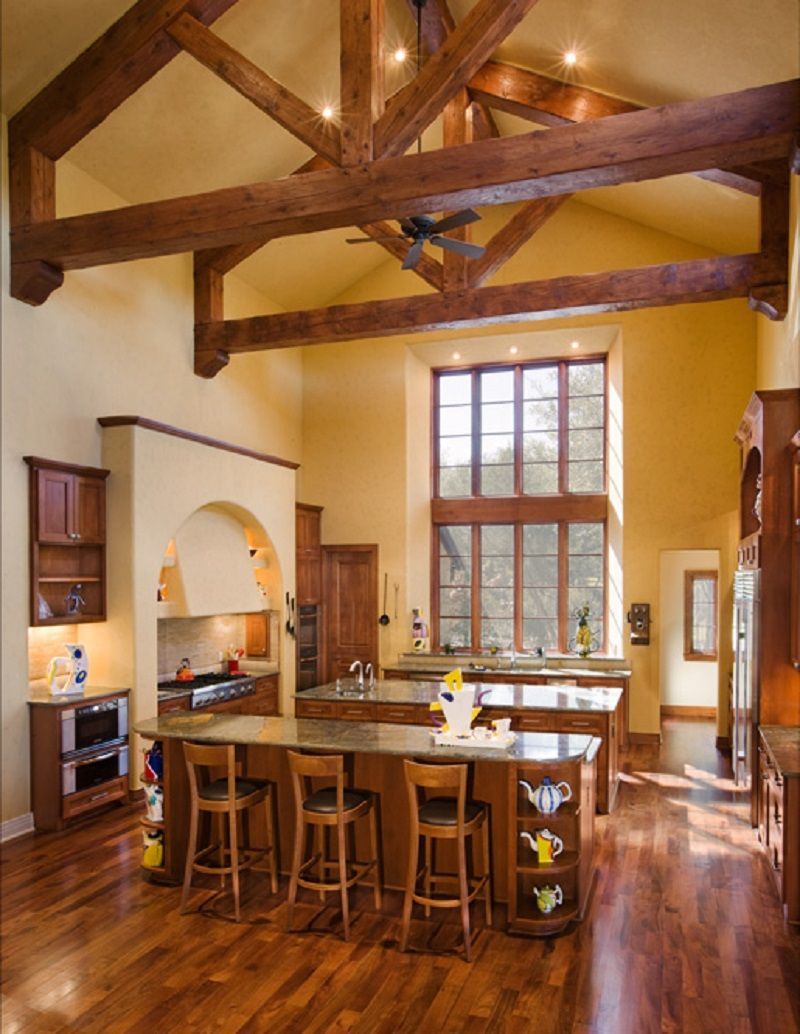 Rustic kitchen with wooden beams, dark cabinets, two islands, and a large window.