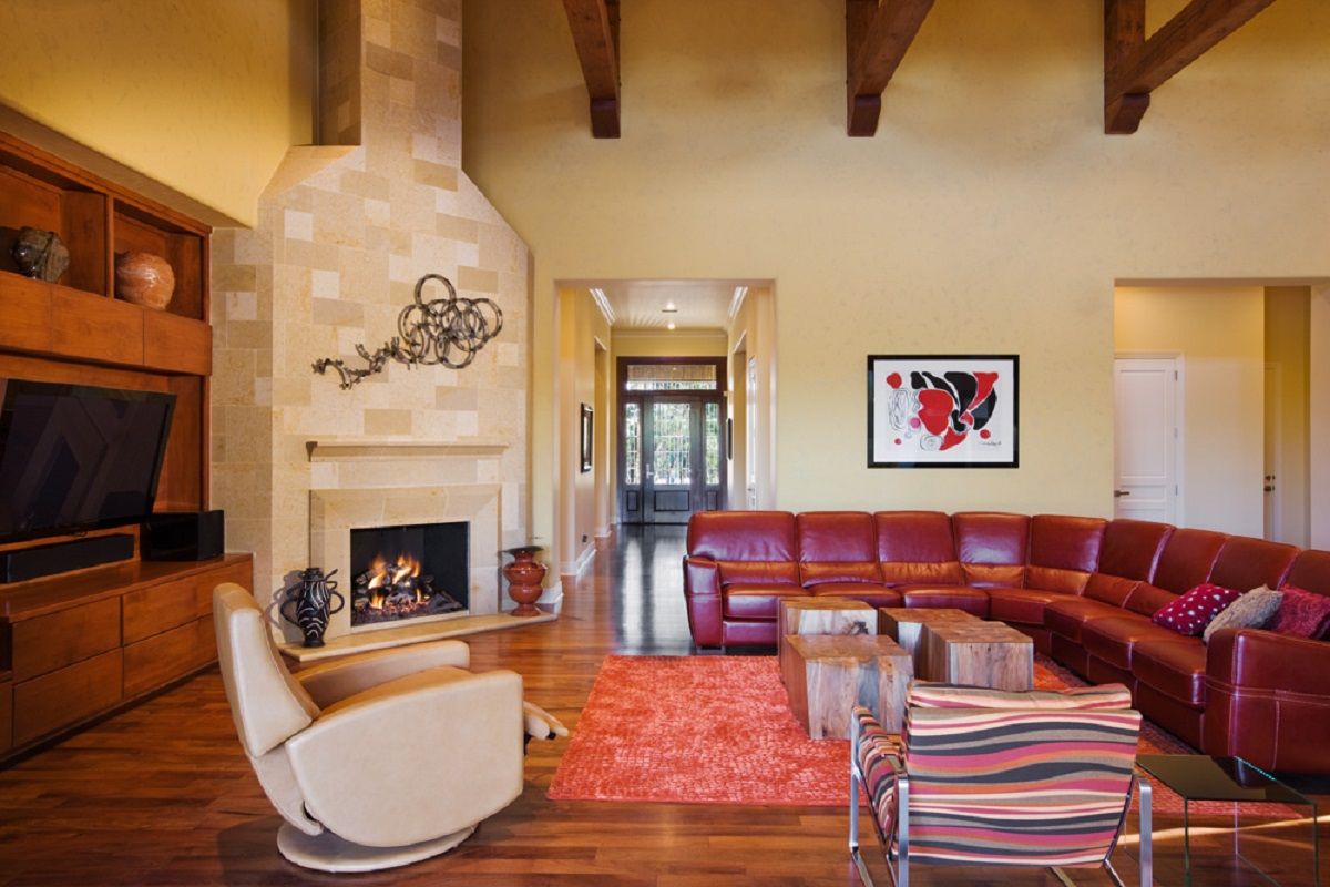Cozy living room with a red leather sectional, fireplace, art, and wooden beams.