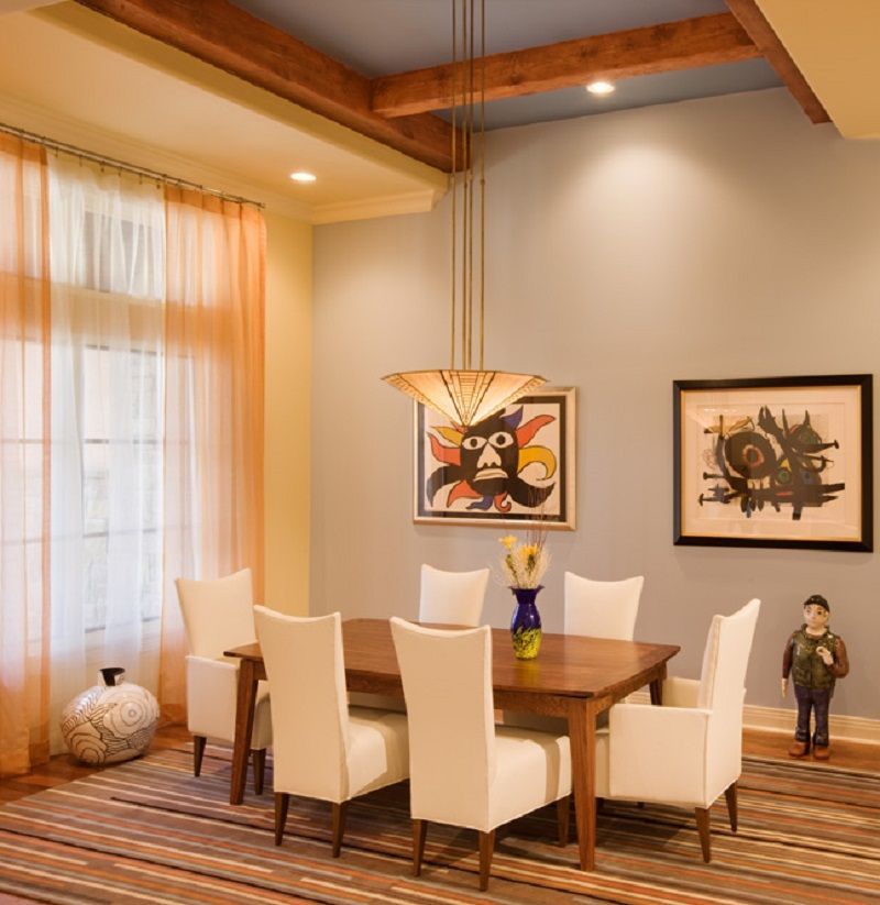 Dining room with modern art, wooden table and white chairs, striped rug, light blue walls.