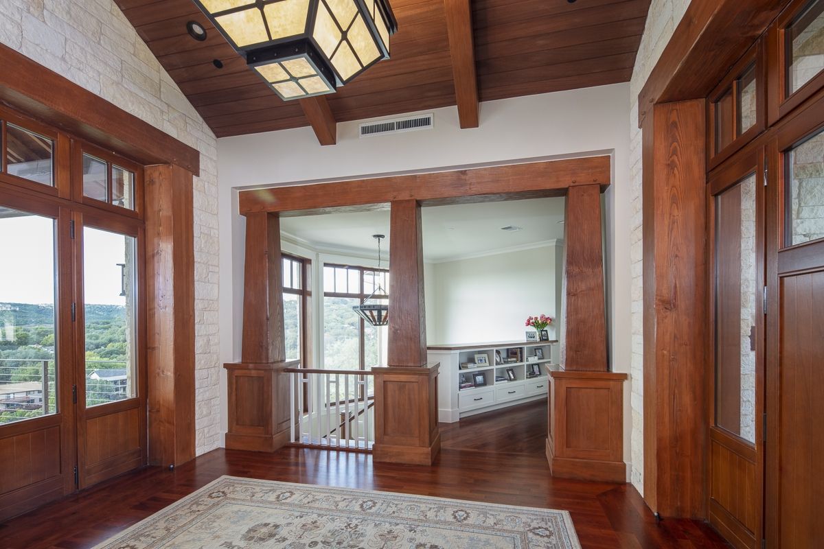 Wooden entryway with dark wood trim and a rug. A view to the outside through the windows and a sunlit room.