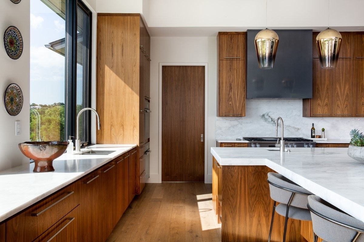 Modern kitchen with wood cabinets, white countertops, and a large window overlooking greenery.