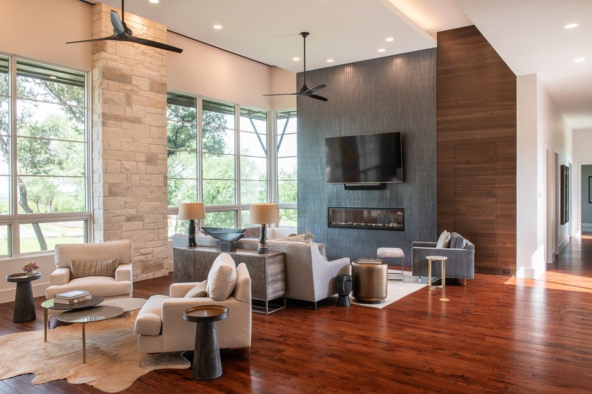 Living room with stone accent wall, fireplace, large windows, wood floors, and modern furniture.