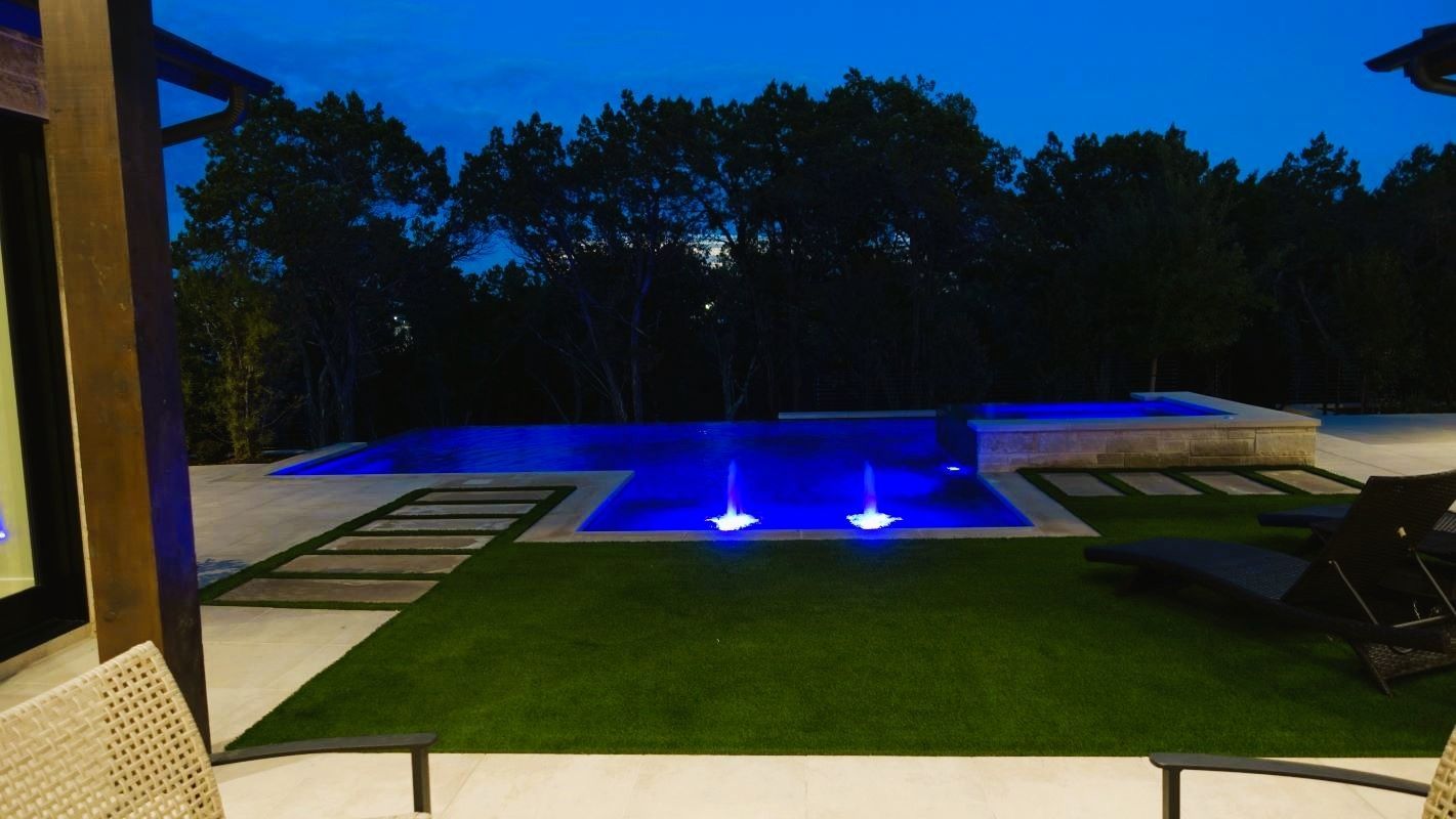 Night view of a pool with blue lights, green grass, and dark trees.