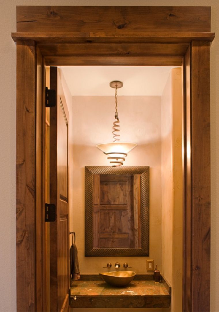 Rustic doorway opening into a powder room with ornate mirror, vessel sink, and pendant light.