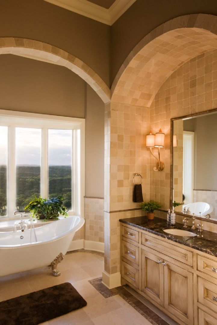 Bathroom with arched doorways, a clawfoot tub, and a vanity. Beige walls, a window with a view, and warm lighting.