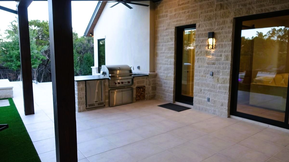 Patio with built-in grill, stone walls, dark doors, and neutral-toned flooring.