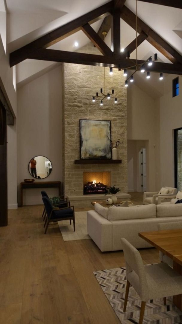 Spacious living room with a stone fireplace, high ceilings, and a modern chandelier.