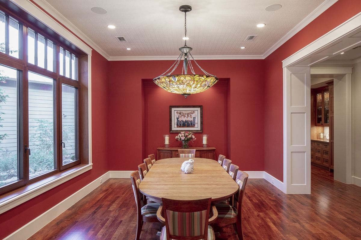 Red dining room with wooden table, chairs, and chandelier. Window on the left, doorway on the right.