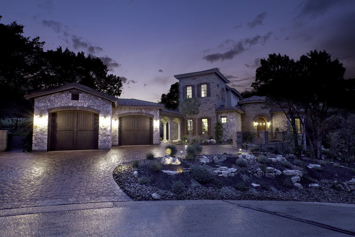 Stone house at dusk with a two-car garage, driveway, and manicured landscaping under a night sky.