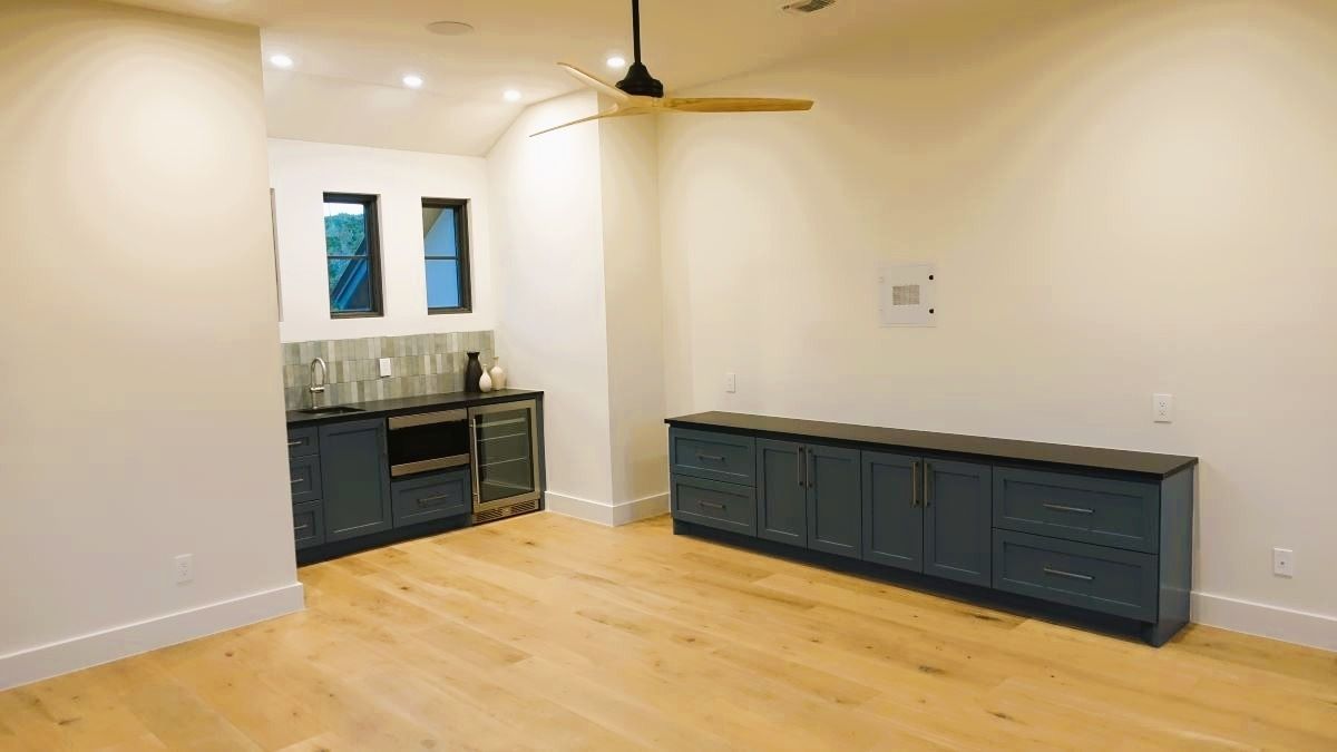 Empty room with wood floor, blue cabinets, and a small bar area with windows.