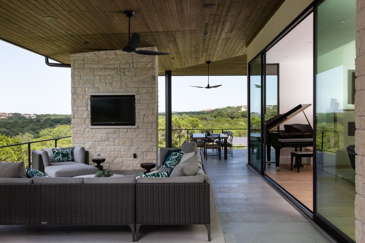 Outdoor patio with seating, TV, and view of a room with a piano, overlooking a landscape.