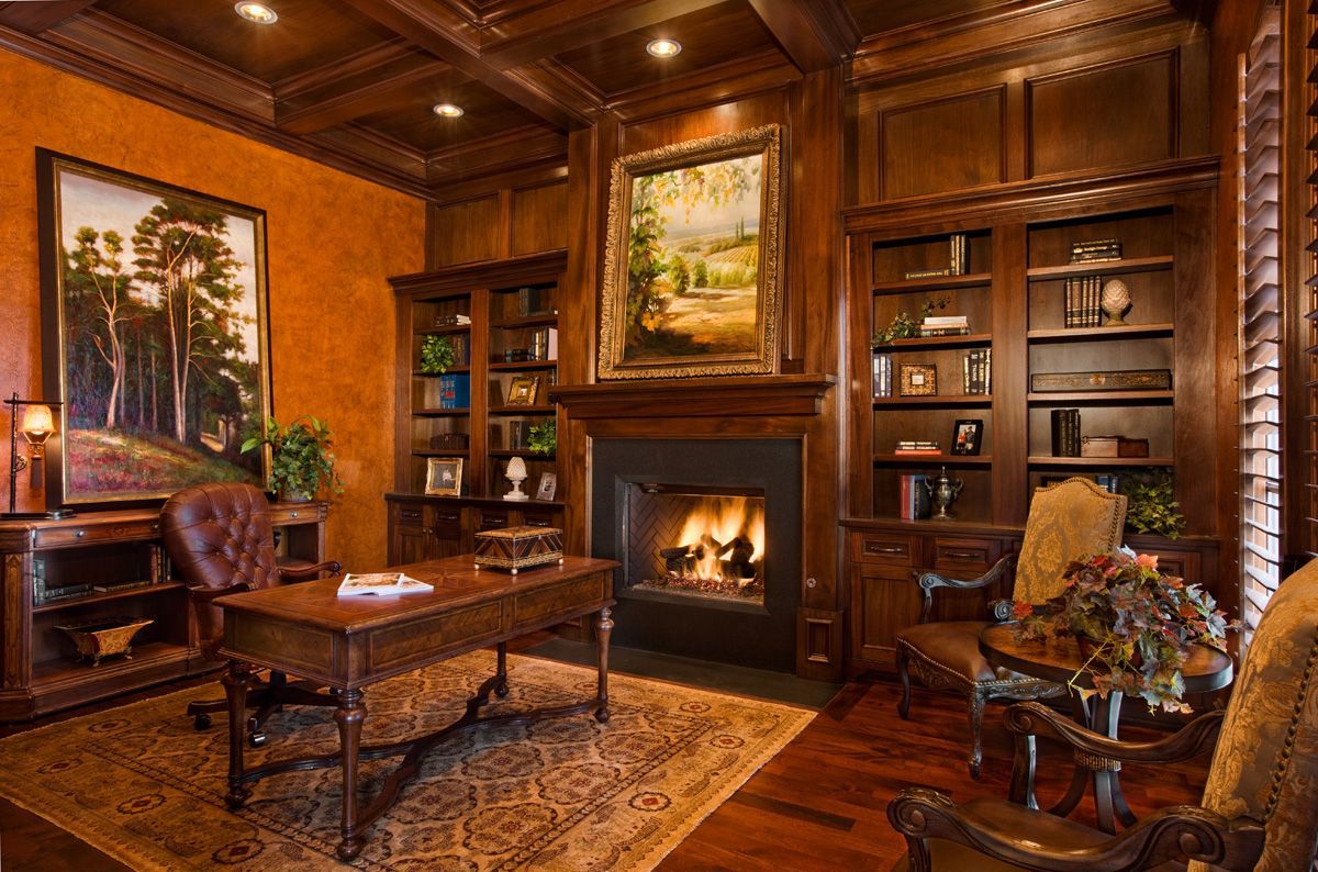 Cozy home office with dark wood furniture, fireplace, paintings, and bookshelves.
