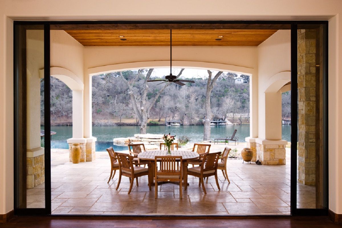 Open-air dining area with a river view; wooden table and chairs, archway, stone pillars, and sliding doors.