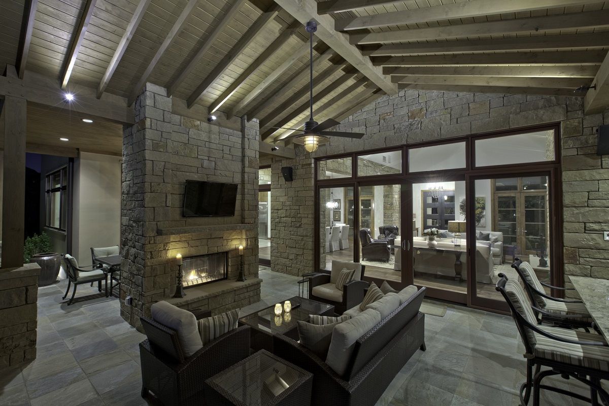 Outdoor living area with fireplace, seating, stone walls, and sliding glass doors.