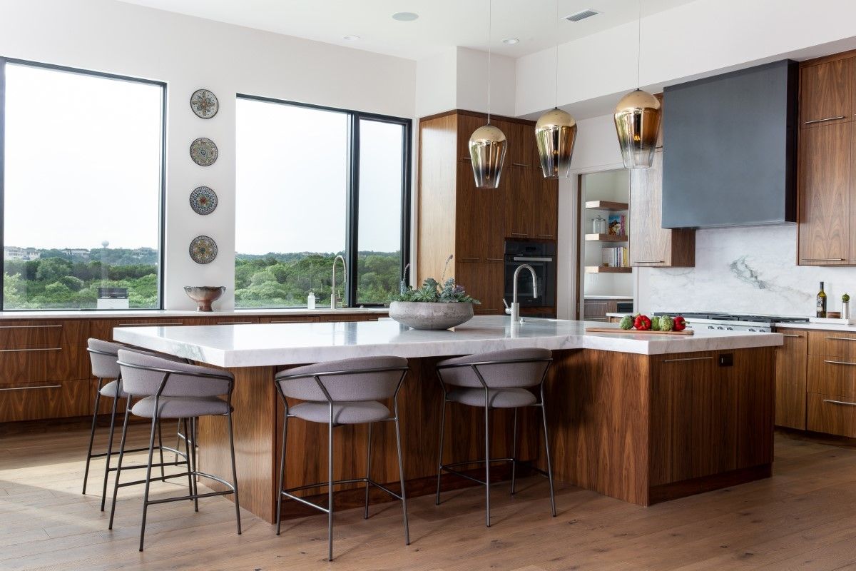 Modern kitchen with walnut cabinets, white countertops, island with bar stools, and large windows.