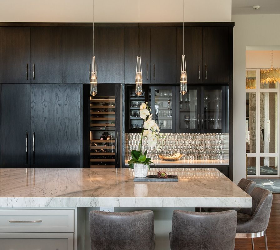 Modern kitchen with dark cabinetry, marble countertop, pendant lights, and wine fridge.