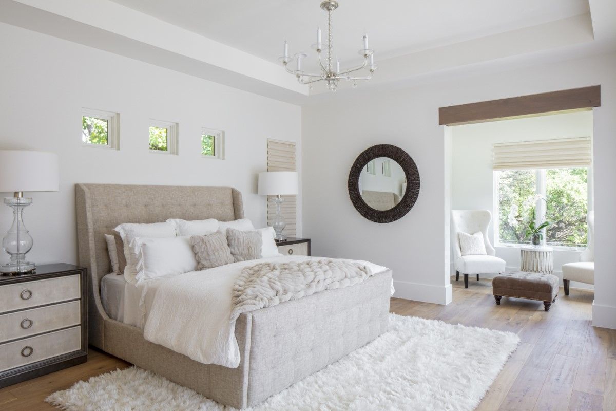Elegant bedroom with neutral tones: bed, rug, round mirror, and window seating.