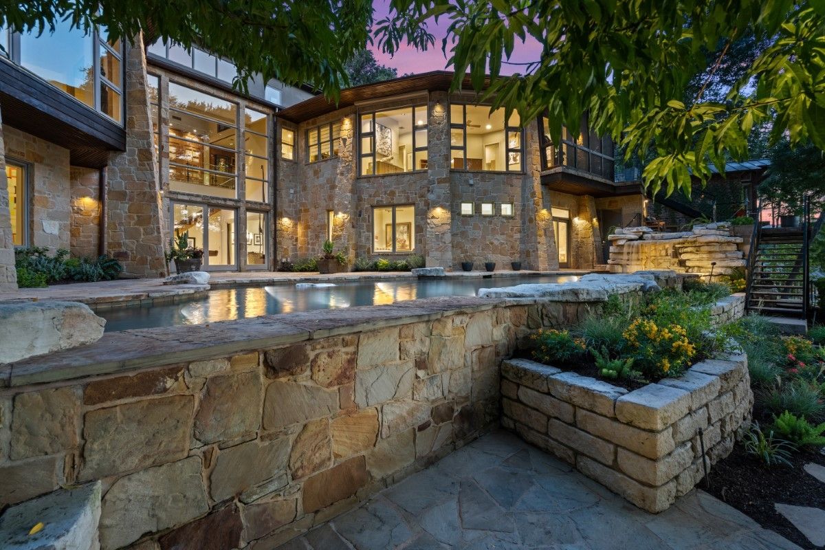 Stone house with pool and landscaping at dusk.