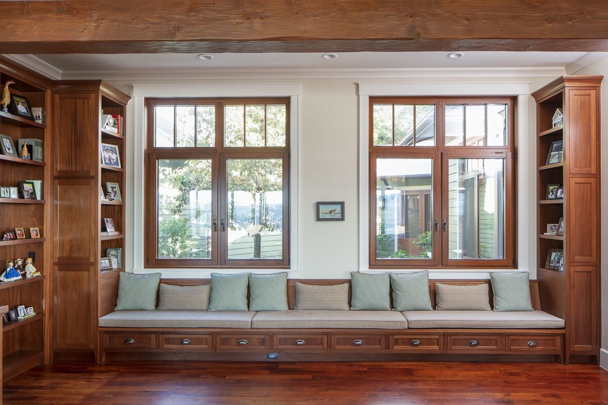 Living room with built-in window seat, bookshelves, two windows, wood trim and flooring.