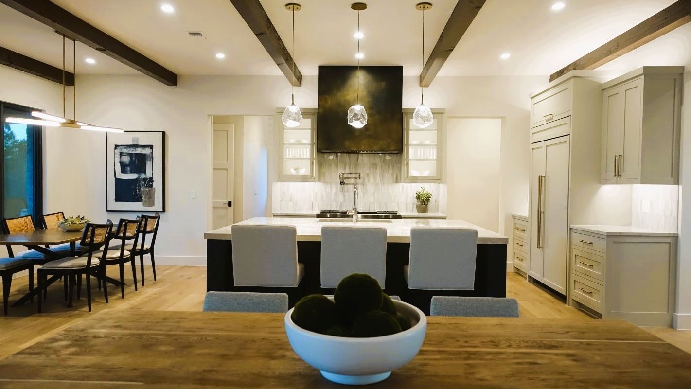 Modern kitchen with island seating and dining area. Wooden beams and light cabinetry.