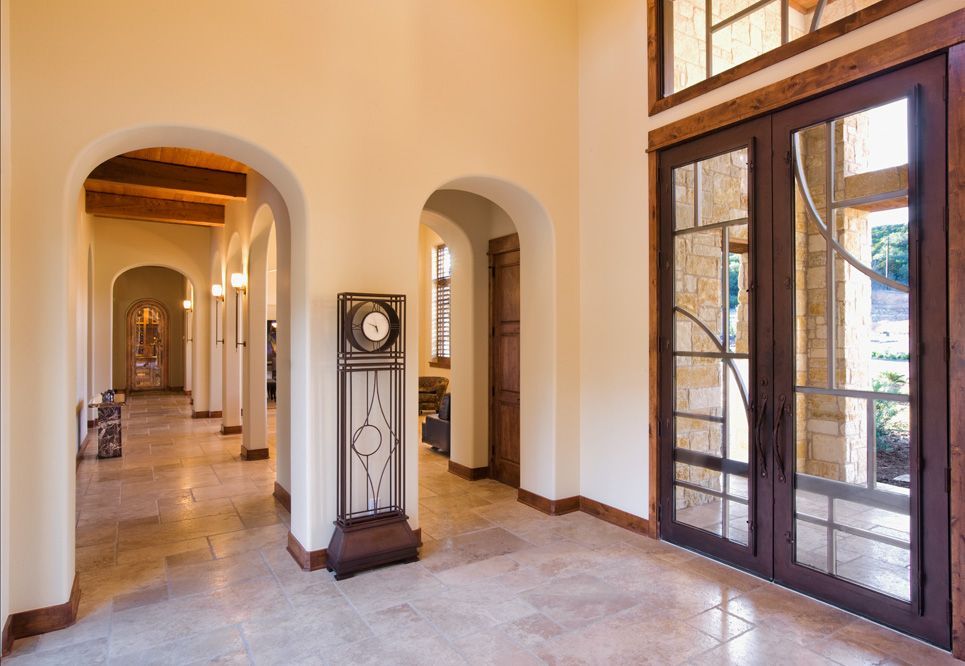 An arched hallway with a grandfather clock, leading to a large entrance with glass doors.