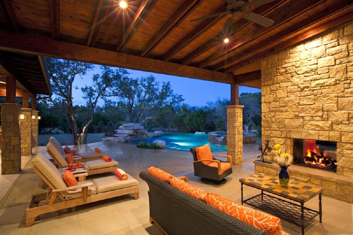 Outdoor patio with fireplace, pool, and seating; stone walls and warm lighting.