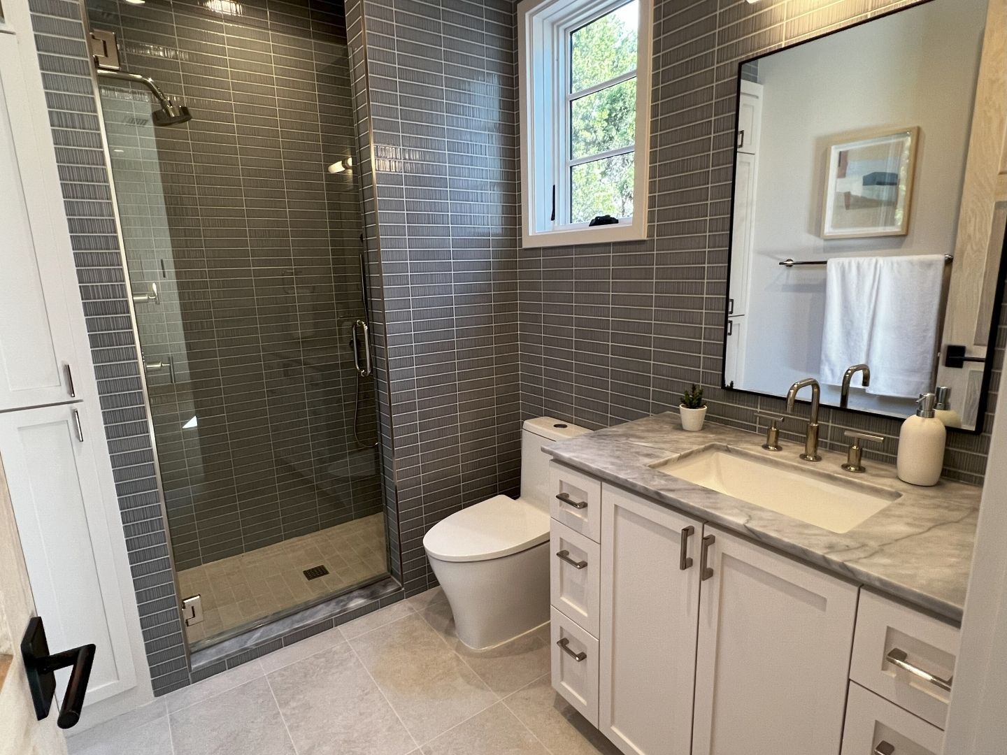 Modern gray tiled bathroom with glass shower, white vanity, and toilet.