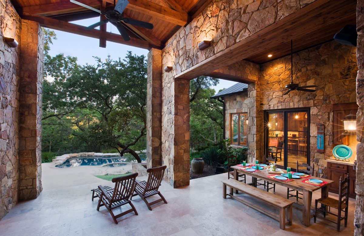 Stone patio with dining table, bench, chairs, and pool overlooking trees.