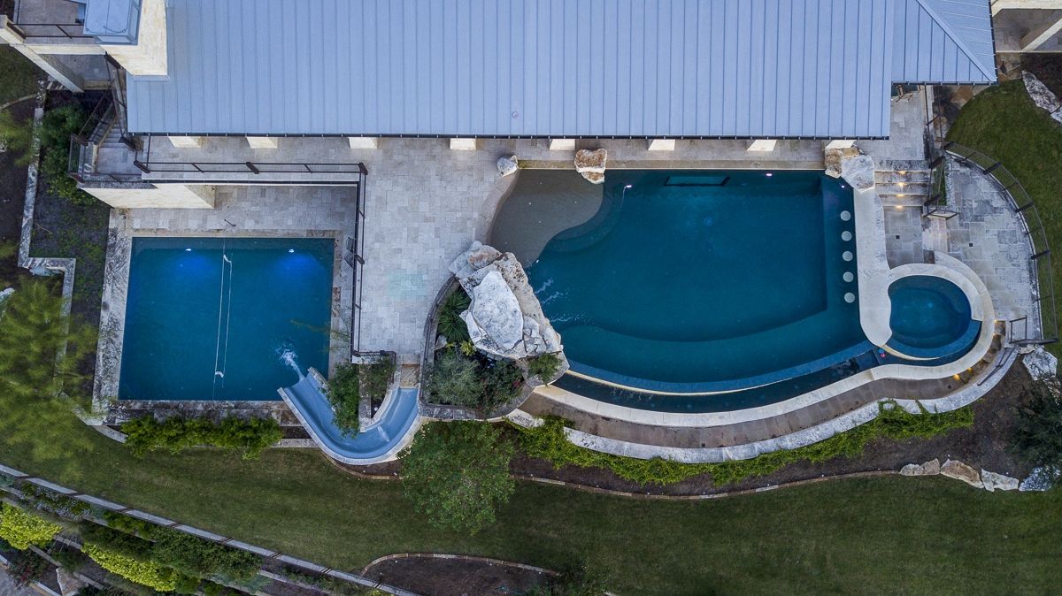 Aerial view of a large pool complex with a lap pool, main pool, slide, and hot tub.