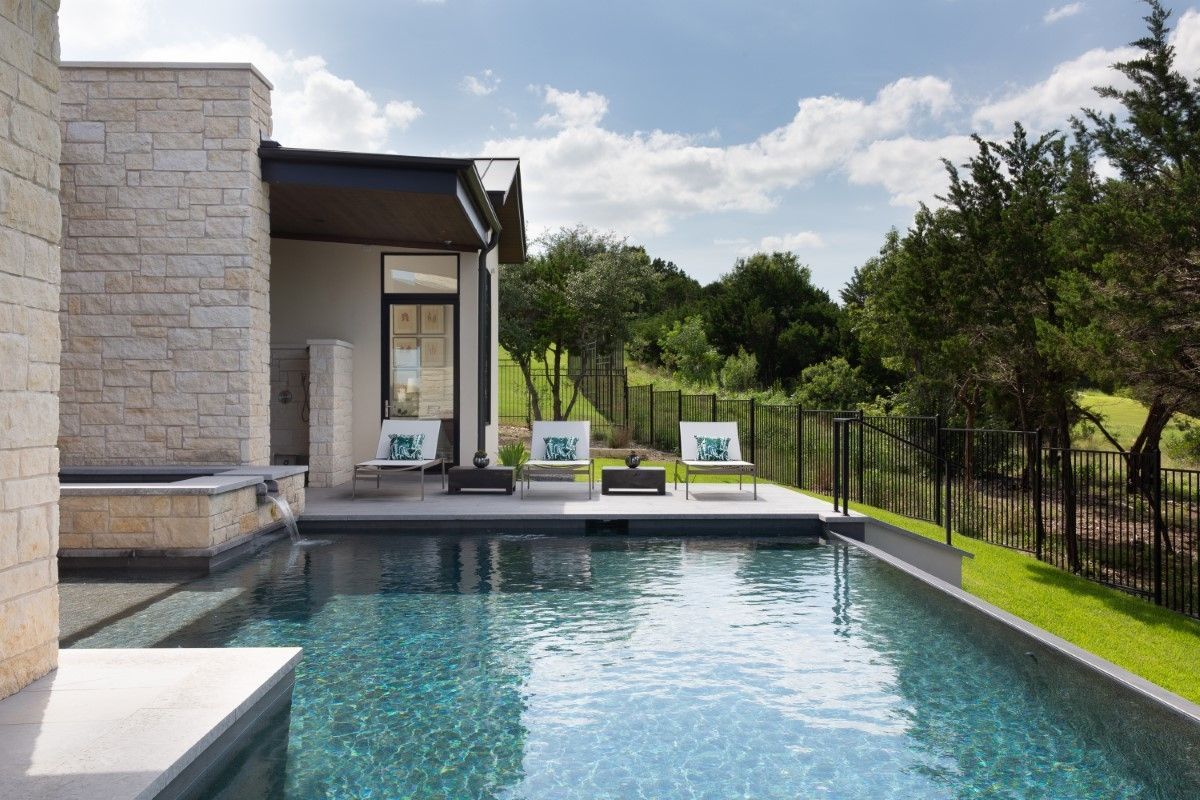 Poolside scene: a modern home with a pool, lounge chairs, and trees under a blue sky.