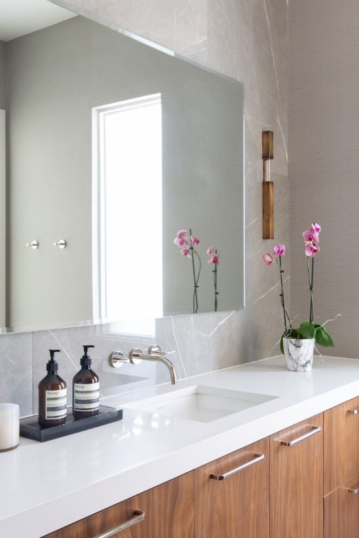 Bathroom with white countertop, wood cabinets, large mirror, and pink orchids.