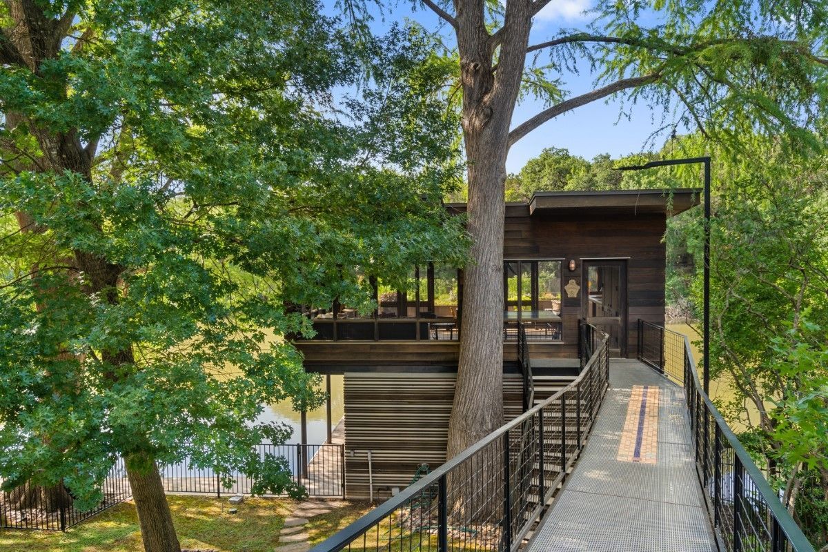 Treehouse with a bridge, surrounded by trees and overlooking water. Brown wood, metal railing.