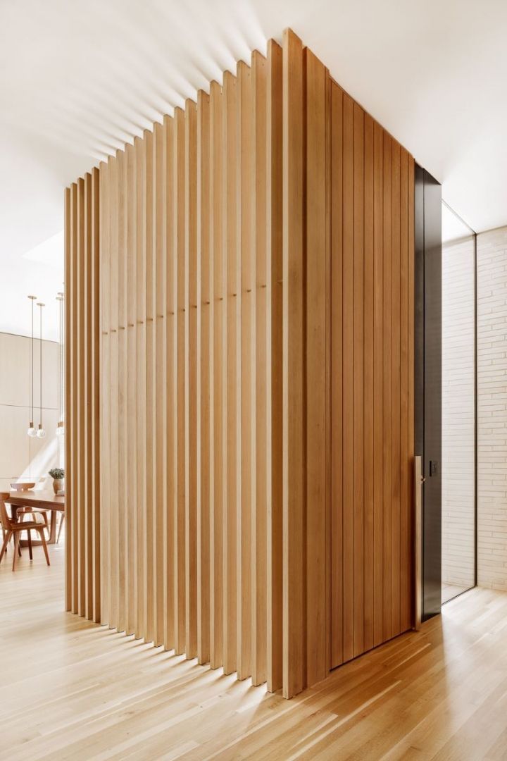 Wooden slatted room divider with a glass-doored entrance, in a light-filled modern home.