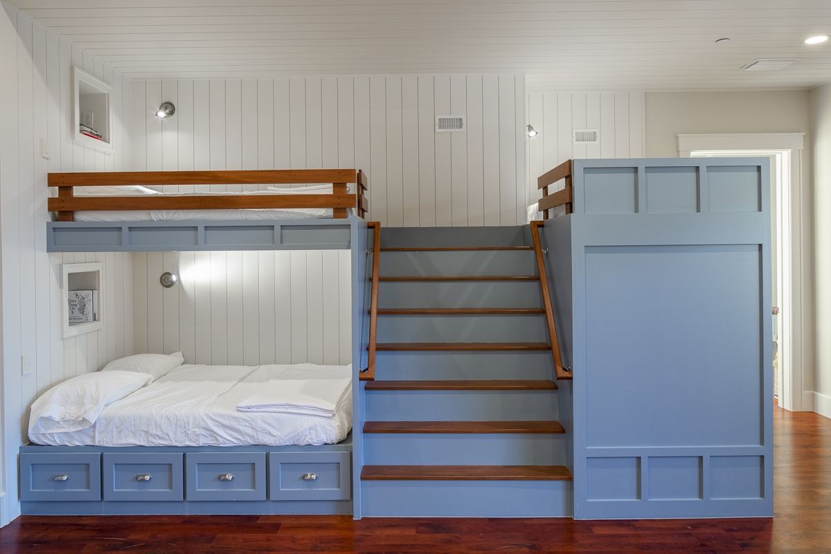Built-in bunk bed with stairs and storage; blue and wood tones. White paneled walls in a room with hardwood floors.