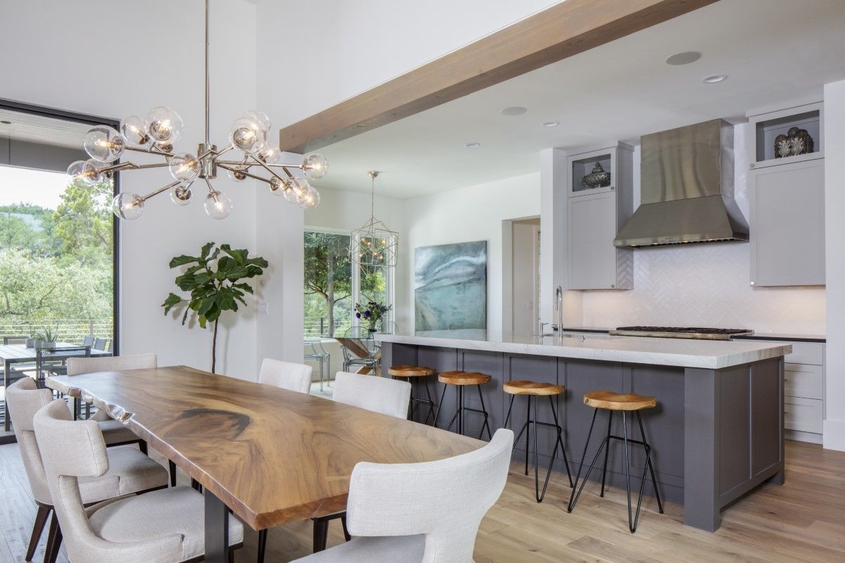 Open-concept kitchen and dining area with a large wooden table, island with bar stools, and modern lighting.