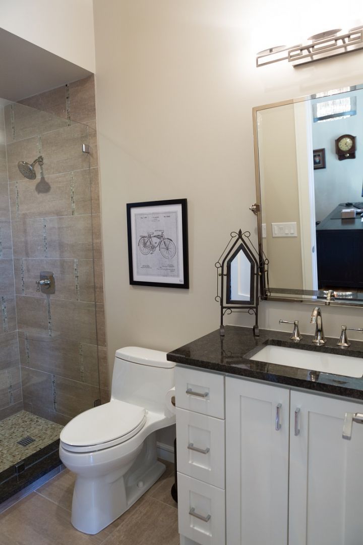 Bathroom with shower, toilet, white vanity, black countertop, framed art, and a mirror.